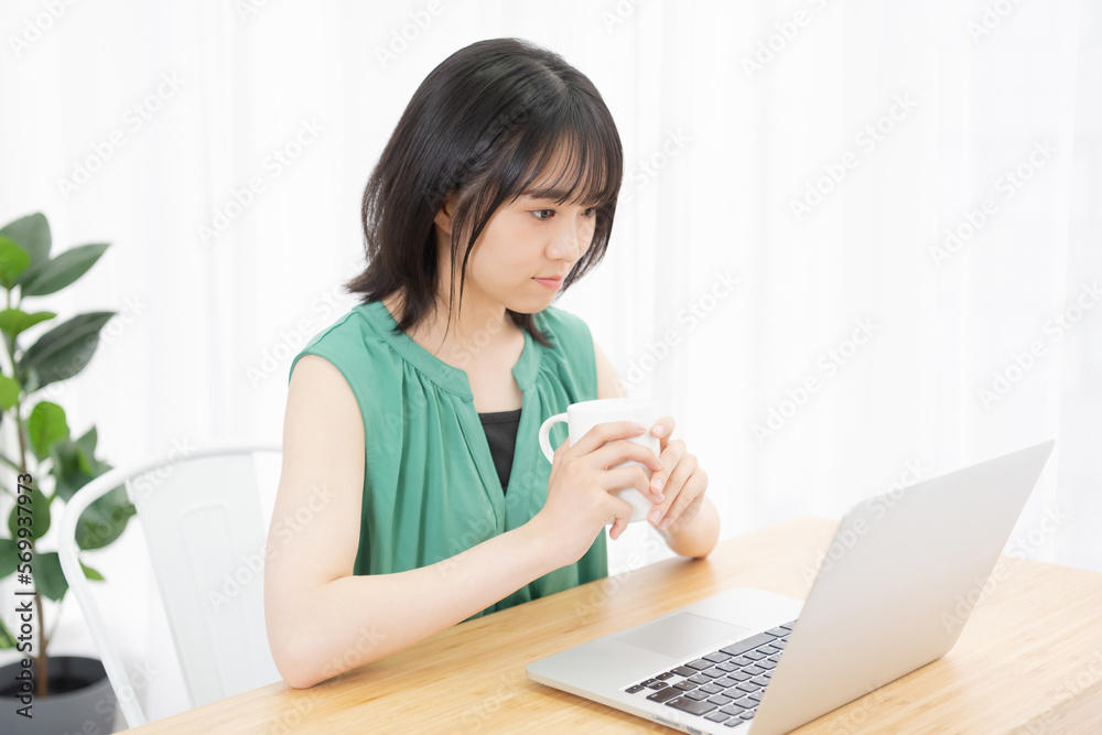 PCを見ながら飲み物を飲んでいる若い女性 PCを見ながら飲み物を飲んでいる若い女性