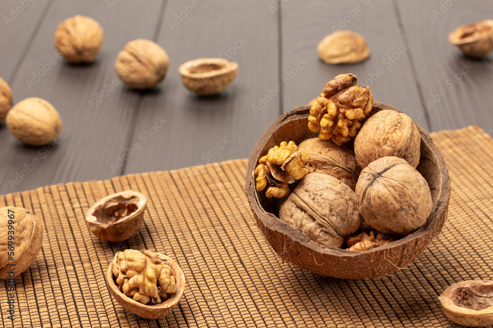 Whole and cracked walnuts in coconut shells on napkin of thin wooden sticks.