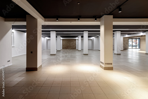A large empty room with ceramic tiles on the floor  a black ceiling with lighting and columns propagating the ceiling