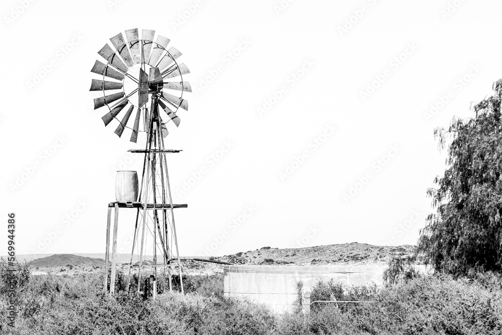 Typical Karoo landscape with windmill, water tank and dam. Monochrome