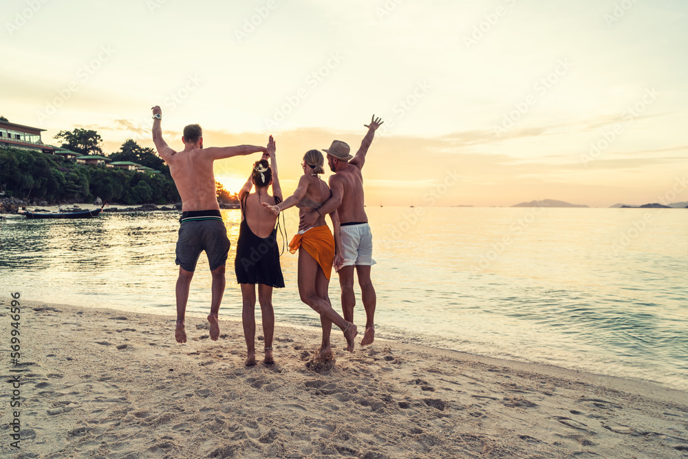 Group of happy friends enjoying beautiful sunset at the tropical beach, jumping and having fun together. Travelers.
