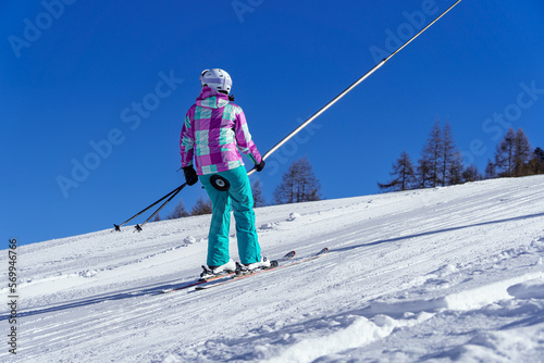 A young girl skier, climbs the slope at a ski resort, using a butt lift or ski lift. French Alps.
