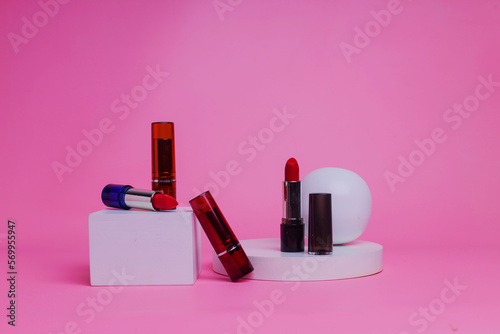Some lipsticks are on the podium on a pink background.