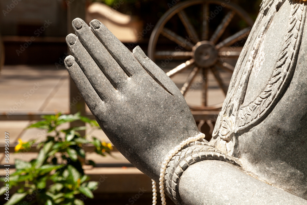 Carved stone statue hands close-up in a Buddhist temple with the wheel of life in the background. Religious sculpture detail, a person making a mudra with their hands