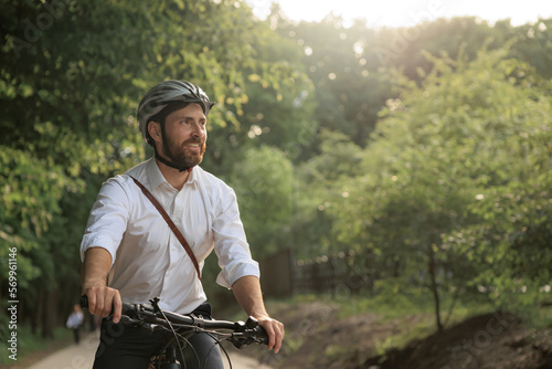 Smiling bearded businessman riding by bike along green alley in morning.