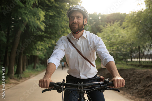 Portrait of joyful male entrepreneur riding by bike through park area. © Tymoshchuk