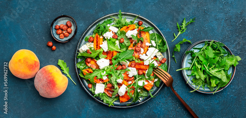 Delicious grilled peach salad with cheese, hazelnuts and arugula on blue background, top view banner