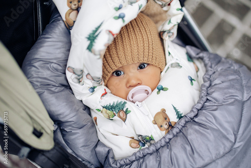 Dressed and wrapped infant lies down in baby carriage during walk in winter.