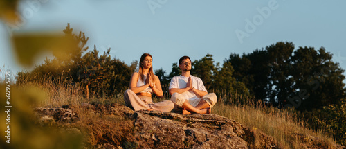 Man and Woman Meditating Outdoors While Sitting on the Rock, Young Adult Couple Practicing Yoga at Sunset © Romvy