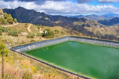 Water reservoir in the mountain agricultural landscape, Andalusia, Spain. Watering for fields, wineyards and orchards.