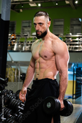 A handsome muscular man with a beard is holding a dumbbell. Sports, healthy lifestyle