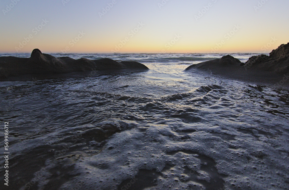 olas del mar entrando por las figuras de la arena, puesta de sol en la playa