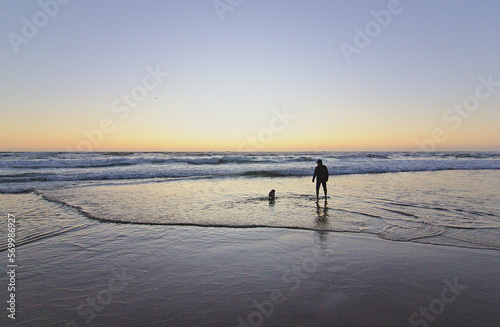 hombre jugando con su perro pug en la orilla del mar mientras esta la puesta de sol