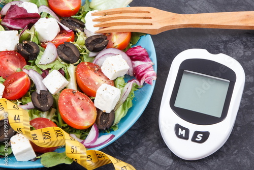 Glucometer, tape measure and greek salad with feta cheese and vegetables. Checking sugar level and slimming