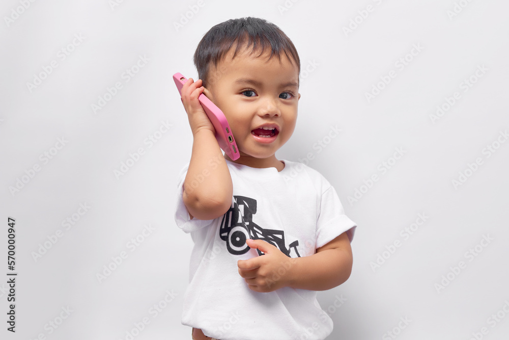 Smiling Toddler Asian kid boy 2 years old wearing a white t-shirt talking on mobile phone with a friend, looking at camera isolated on white background Smiling Toddler Asian kid boy 2 years old wearing a white t-shirt talking on mobile phone with a friend, looking at camera isolated on white background