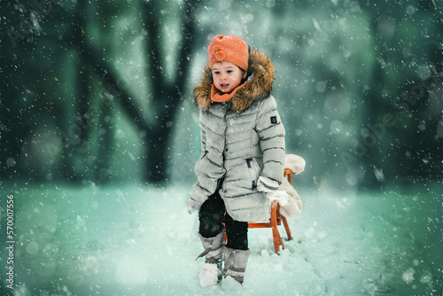 Warm clothing and no winter for me. Warm clothed child pulling sled through snowflakes during the winter snowy day.