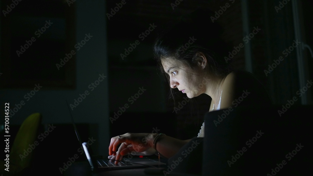Woman working at night in the dark at home with glowing light on face Woman working at night in the dark at home with glowing light on face