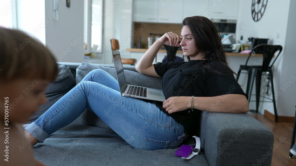 Mother sitting on couch using laptop with baby toddler. Parent multi tasking working from home with child. Motherhood lifestyle Mother sitting on couch using laptop with baby toddler. Parent multi tasking working from home with child. Motherhood lifestyle