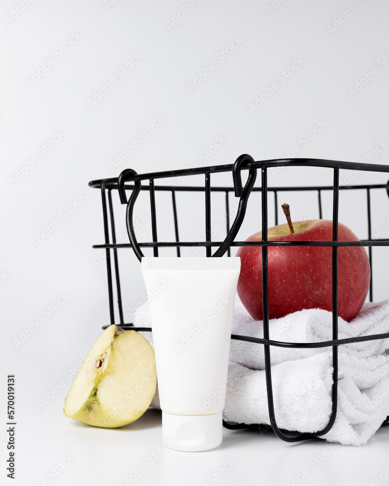 A tube of cream next to a basket with white towels and apples A tube of cream next to a basket with white towels and apples