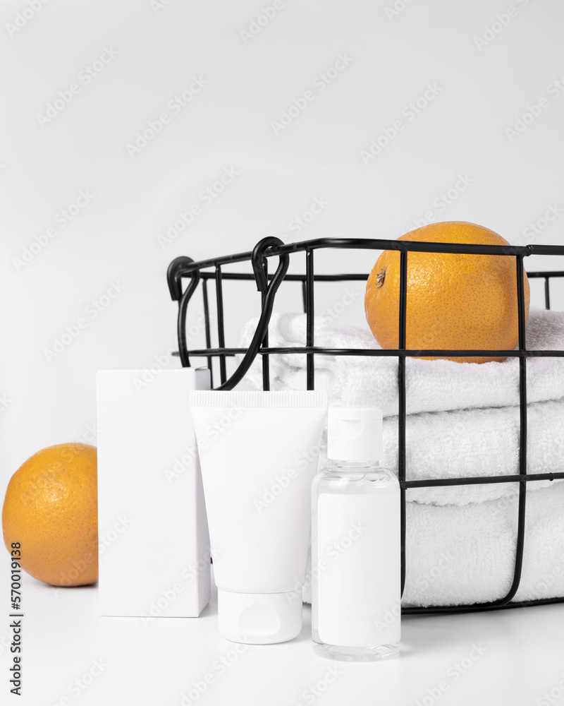 Several tubes of cosmetics next to a basket in which towels and oranges