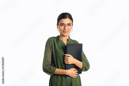A young modern confident Indian Asian Businesswoman or female secretary or corporate office employee wearing eyeglasses holding a file standing and looking at the camera isolated on white background.