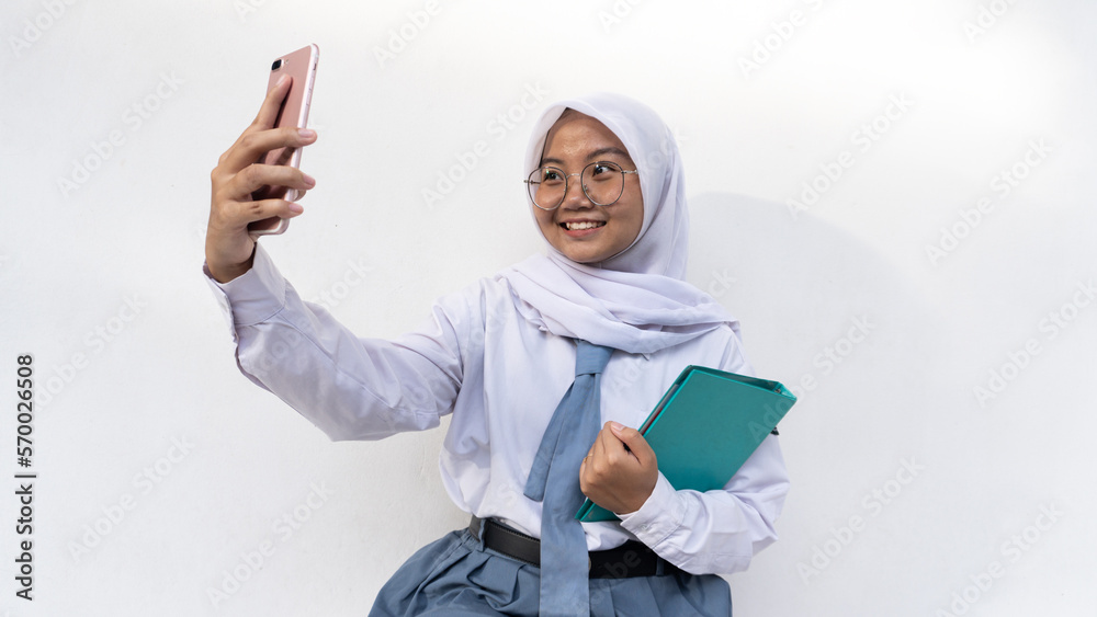 Indonesian female high school students in gray and white uniforms taking a selfie and holding a notebook Indonesian female high school students in gray and white uniforms taking a selfie and holding a notebook