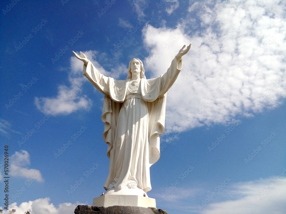 Statua del Sacro Cuore di Gesù su cielo azzurro punteggiato da