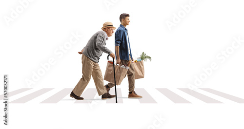 Full length profile shot of a young man helping a senior with grocery bags on a pedestrian crossing