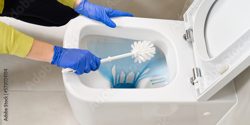 Wall mounted toilet cleaning with detergent. Woman hotel maid cleans a bathroom toilet with a scrub brush. household service. Modern flush toilet. Cleaning photo