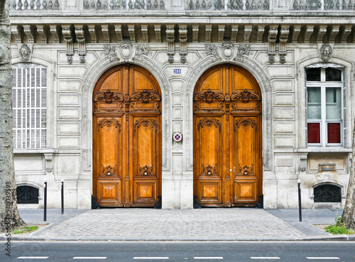 Paris ancient stone building entrance with carved doors, stone walls and balcony with trees in front