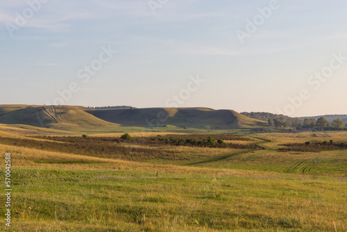 a grassy field with hill with forests in the distance. Rural scene country road and old farm in countryside