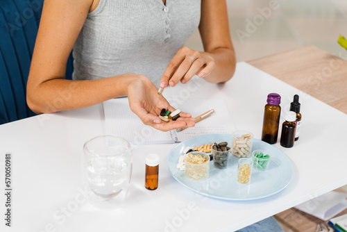 Nutritionist is holding different dietary supplement pills in her hands and writing prescription for daily tablets intake for client for health care.