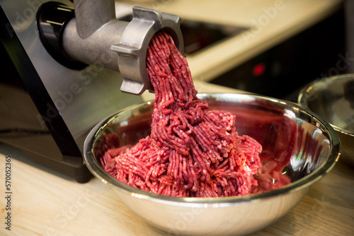 Minced meat comes out of the mincer in a metal bowl