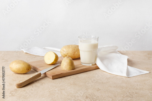 A glass of potato milk stands on a wooden board. There are unpeeled fresh potatoes nearby. Vegan product, vegetable milk. Copy space, horizontal orientation.