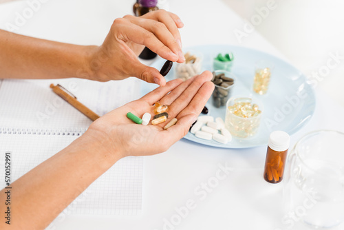 Nutritionist is holding different dietary supplement pills in her hands and writing prescription for daily tablets intake for client for health care.