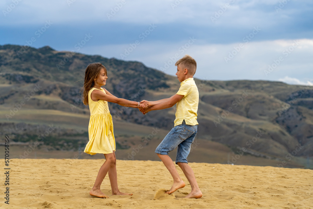 Cheerful boy and girl, holding hands, defiantly spin in the sand dunes and scatter to the sides with laughter and jump