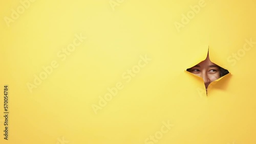 Curious look. Exciting expectation. Coming soon. Tricky woman eyes peeking out from yellow breakthrough hole ripped paper wall copy space background. photo