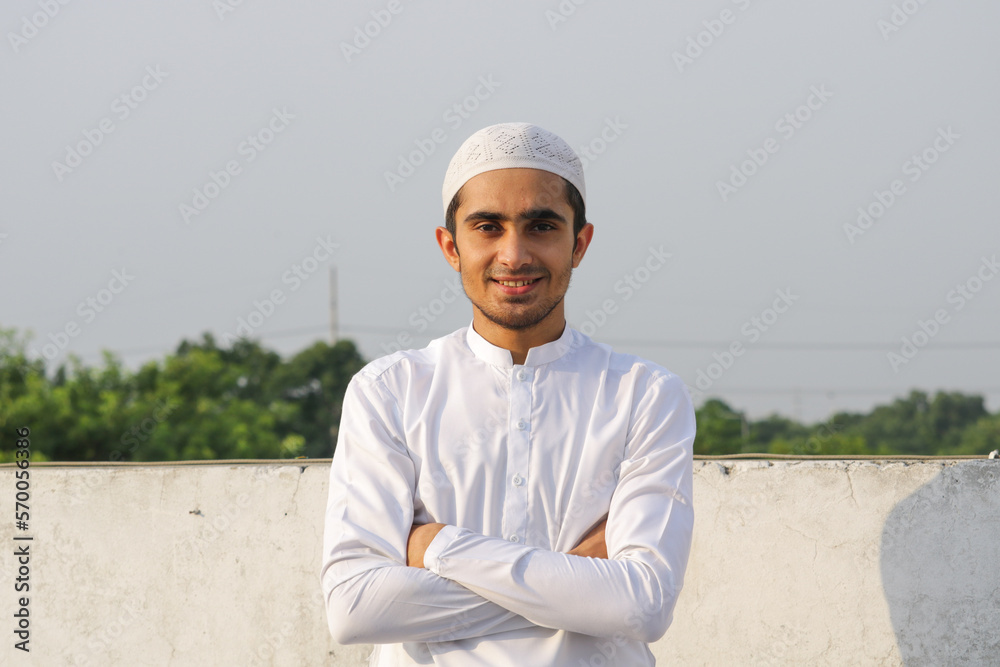 Young Asian Muslim boy looking at the camera wearing white shalwar kameez and cap. Muslim guy smiling wearing shalwar kameez. Young Asian Muslim boy looking at the camera wearing white shalwar kameez and cap. Muslim guy smiling wearing shalwar kameez.