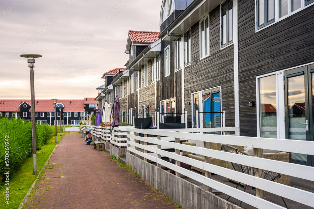 Wooden terraced houses along a cobblestone footpath in a housing development under cloudy sky at sunset