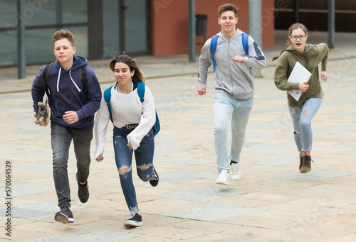Group of cheerful glad students running outdoors in city street on good weather