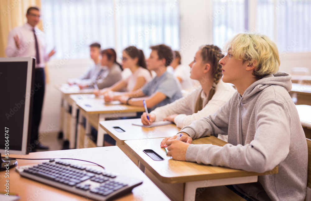 Group of teenage high school students diligently working in class, making notes of teacher lecture