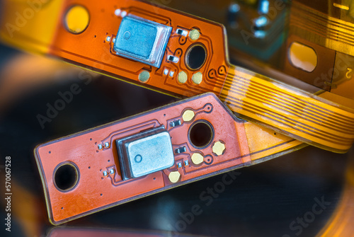 Beautiful flex electronic printed circuits on yellow and orange colored strips on black blurry background. Closeup of bendy PCB or small components on flexible ribbon cables from inside of headphones. photo