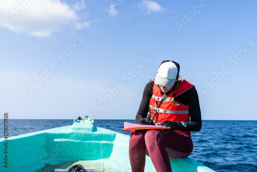 Marine biologist writing down data sitting on a boat photo