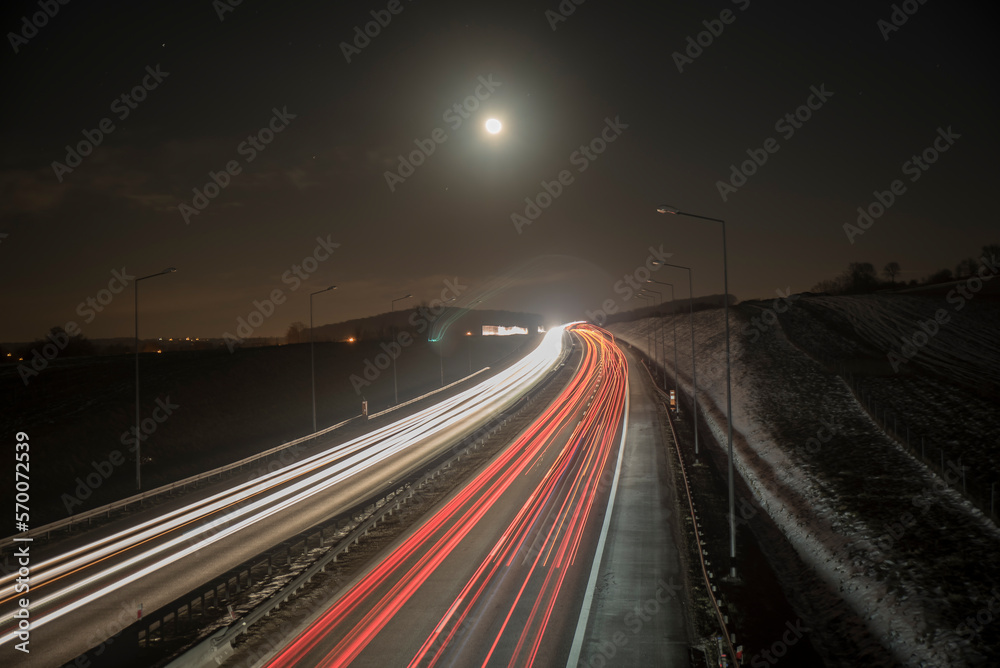 smugi świateł jadących nocą aut autostradą w świetle księżyca