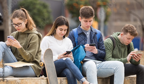 Teenage friends spending time together using smartphones outdoors © JackF