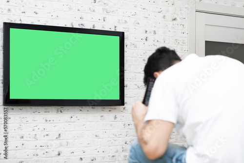 Shocked man on the couch watching tv. Bad news and Green screen concept 