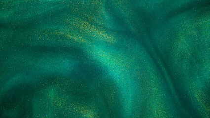 Abstract magic green background with golden sparkles. Photo of a green liquid with gold glitters. Various shades of green with golden splashes. Green backdrop with tints of golden glitters.
