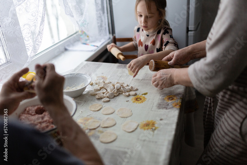 Little girl helping her grandmother with cooking russian dumplings at home