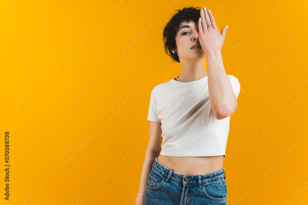 Serious young woman looking at camera with one eye. Female activist covering face with one hand. Medium studio shot. Orange background. . High quality photo Serious young woman looking at camera with one eye. Female activist covering face with one hand. Medium studio shot. Orange background. . High quality photo