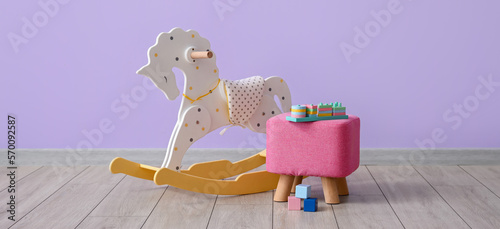 Rocking horse and pouf with toys near lilac wall in room photo